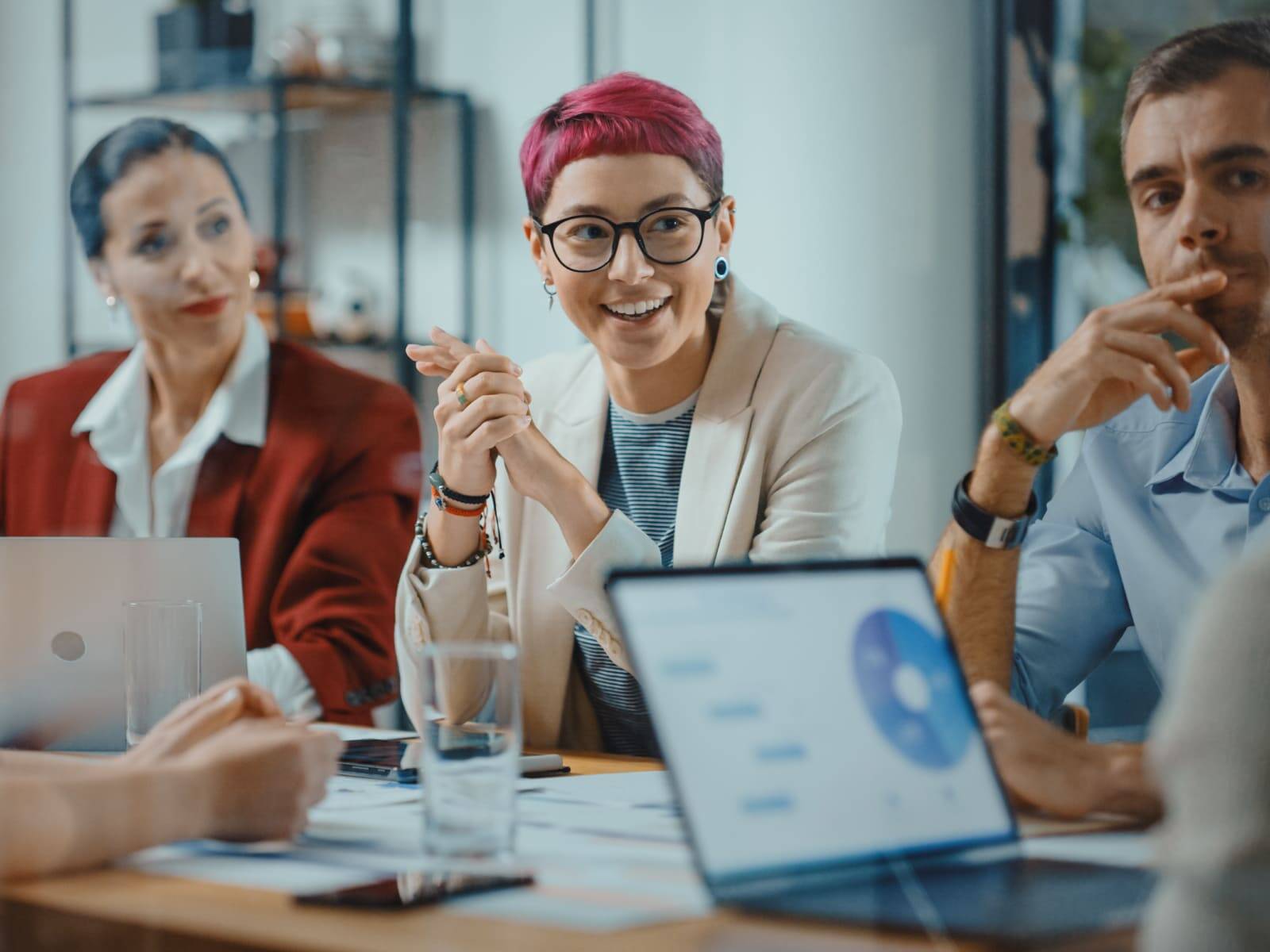 Smiling businesswoman with short pink hair participating in a meeting, with a male colleague listening attentively beside her